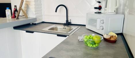 Una cocina moderna con un lavamanos integrado, un microondas y un tazón de manzanas verdes.
