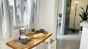 A dining area with a wooden table, white chairs, a window with curtains, a lamp, and a view into another room. - Apartamento Caribe Panama by At Home Costa del Sol (Nerja)