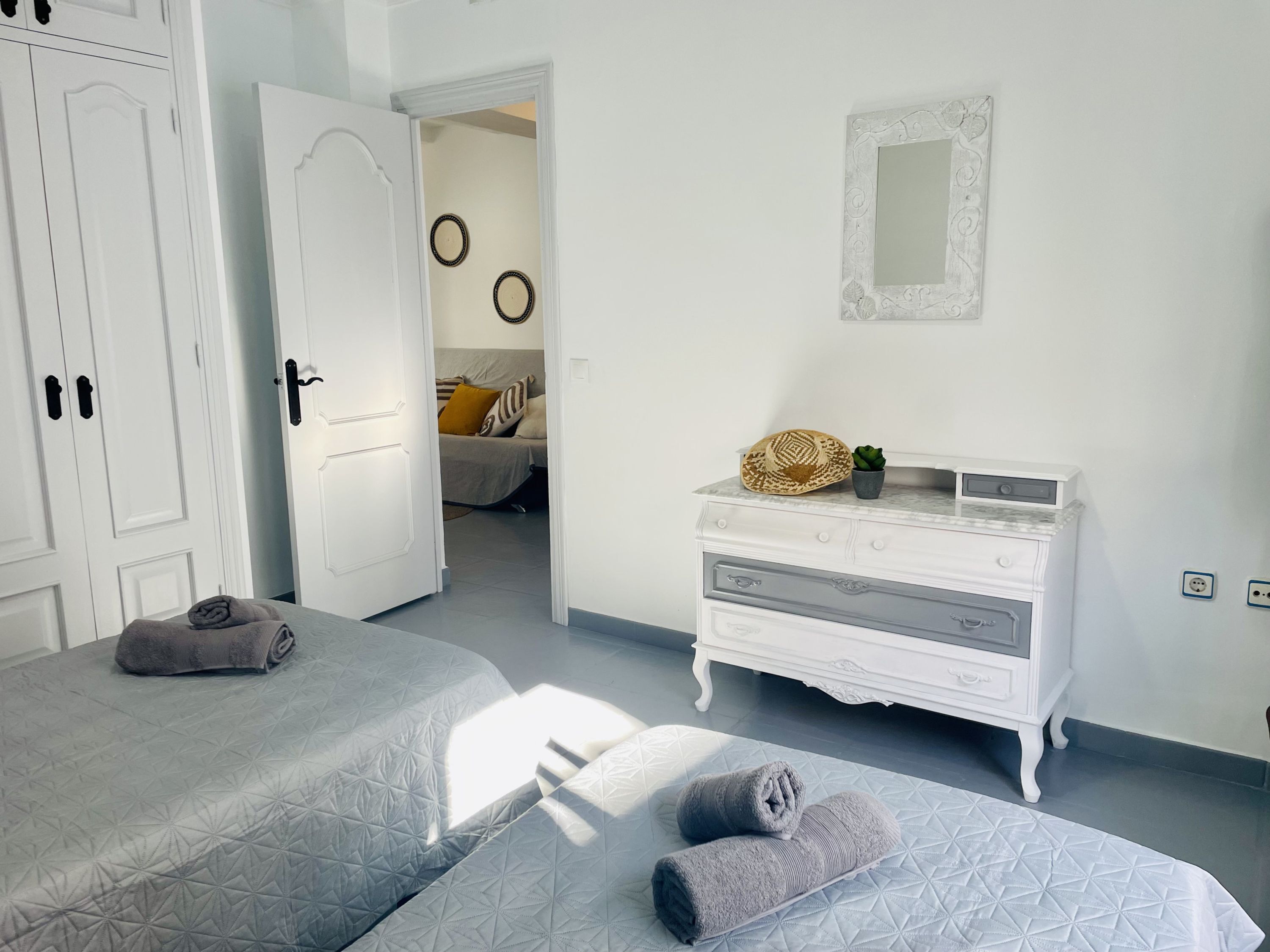Habitación de hotel con dos camas, un aparador, un espejo y una puerta que da a otra habitación.