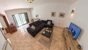 Sala de estar com sofá seccional, mesa de centro, televisão e uma grande janela com vista.