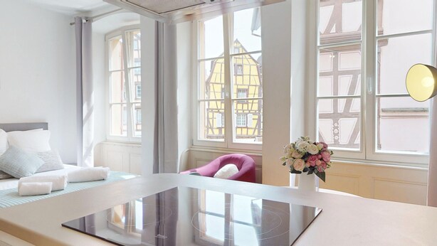 Ett modernt hotellrum med en säng, ett skrivbord, en stol och utsikt över traditionella byggnader genom stora fönster.