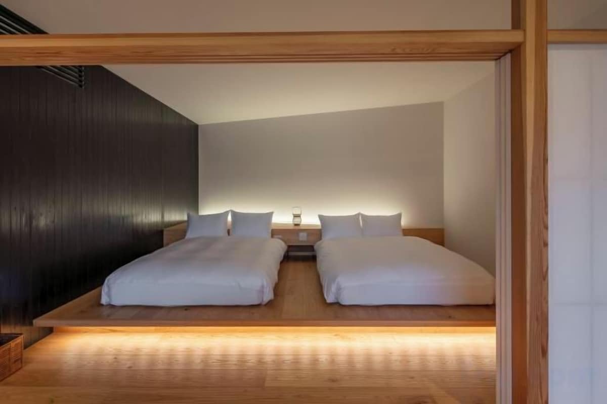 A bedroom with two beds, wooden flooring, and a dark accent wall.
