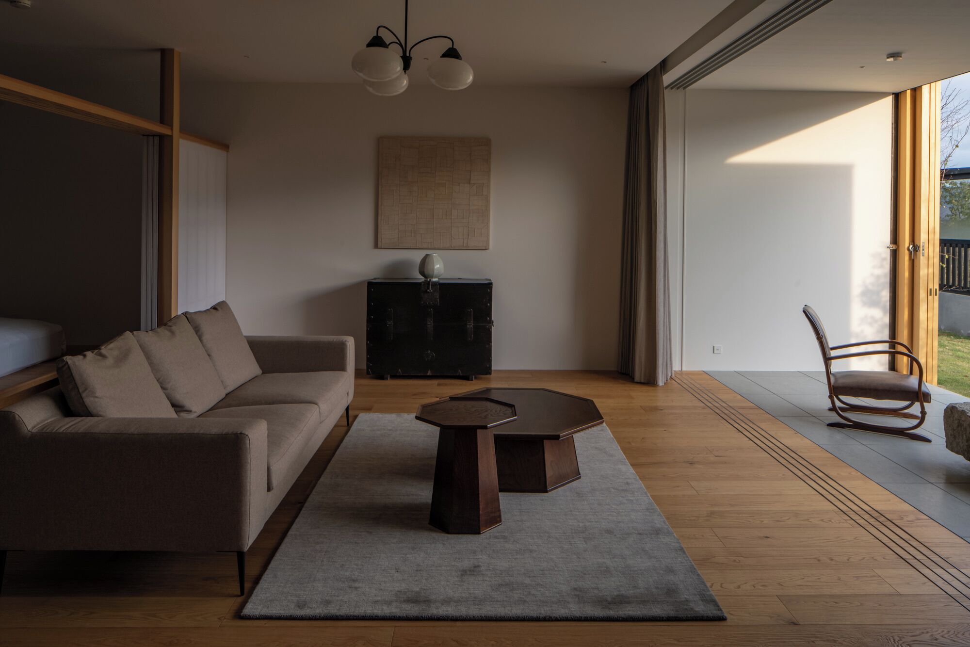 A modern living room with a sofa, a coffee table, and a chair. There is a painting on the wall and a cabinet with a vase.