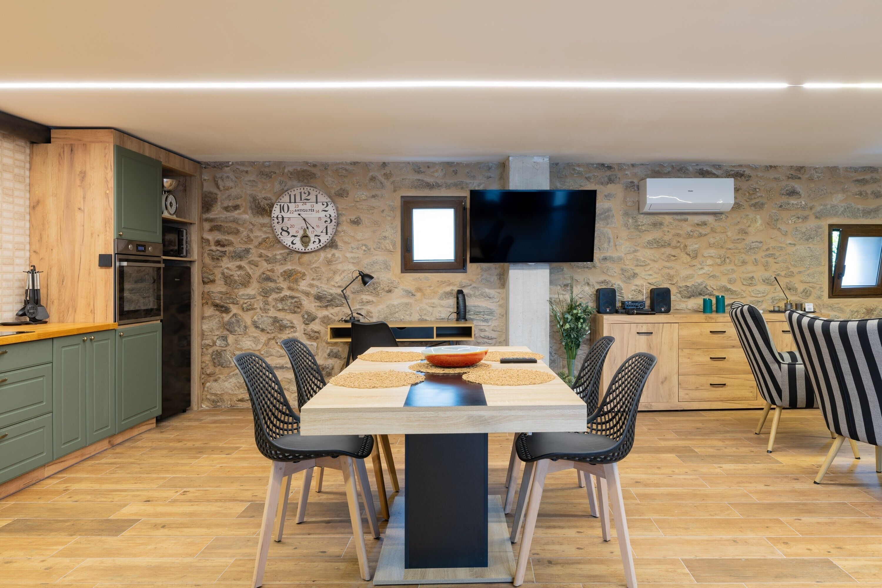 Una cocina moderna con pared de piedra, electrodomésticos integrados y una zona de comedor con mesa y sillas.