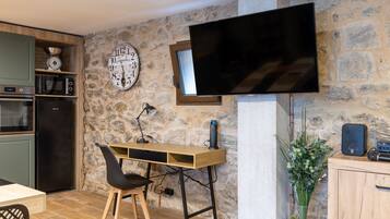Una cucina con parete in pietra, una scrivania in legno, una TV e un'area pranzo con sedie.
