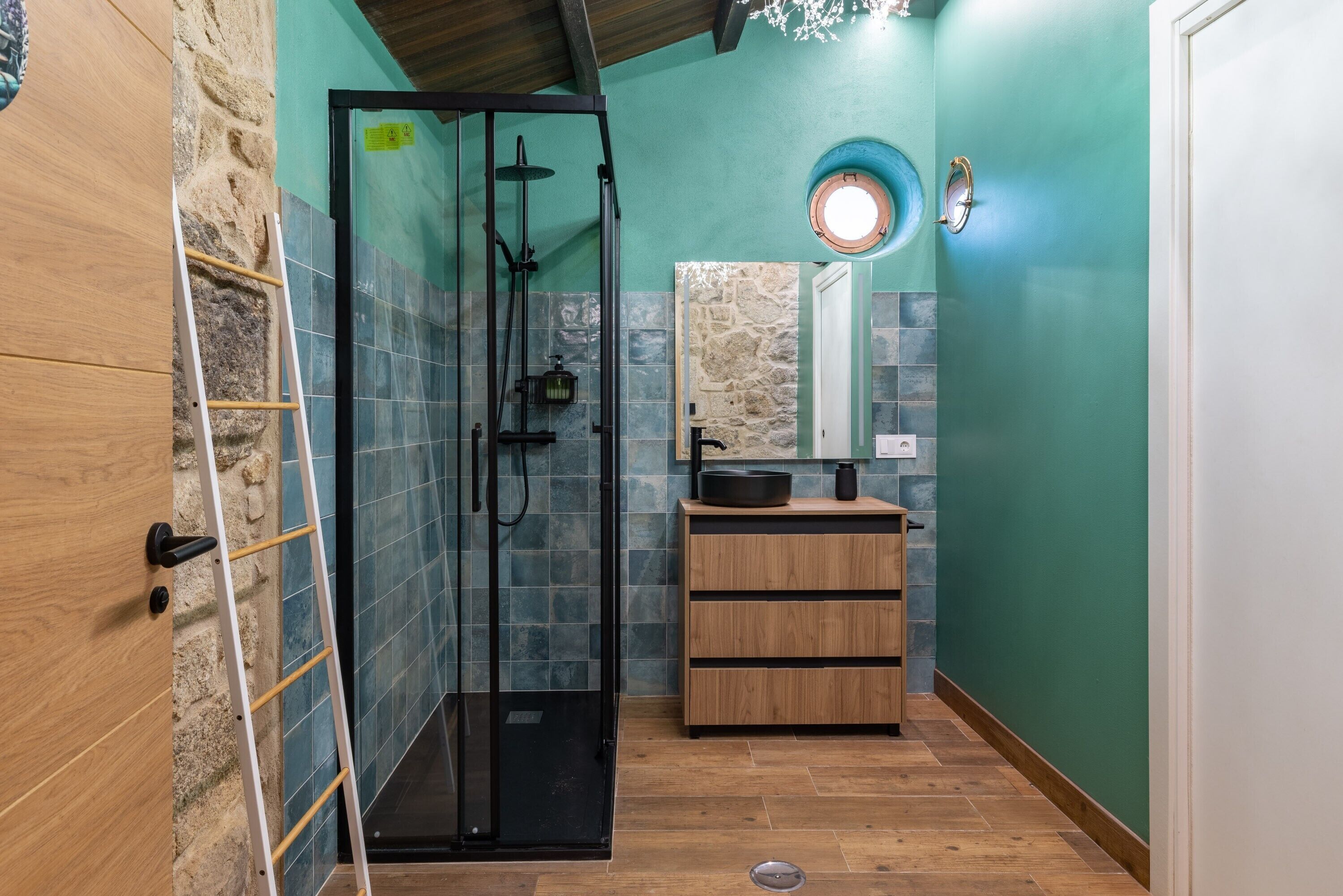 A bathroom with a glass shower enclosure, a wooden vanity, and a stone wall.