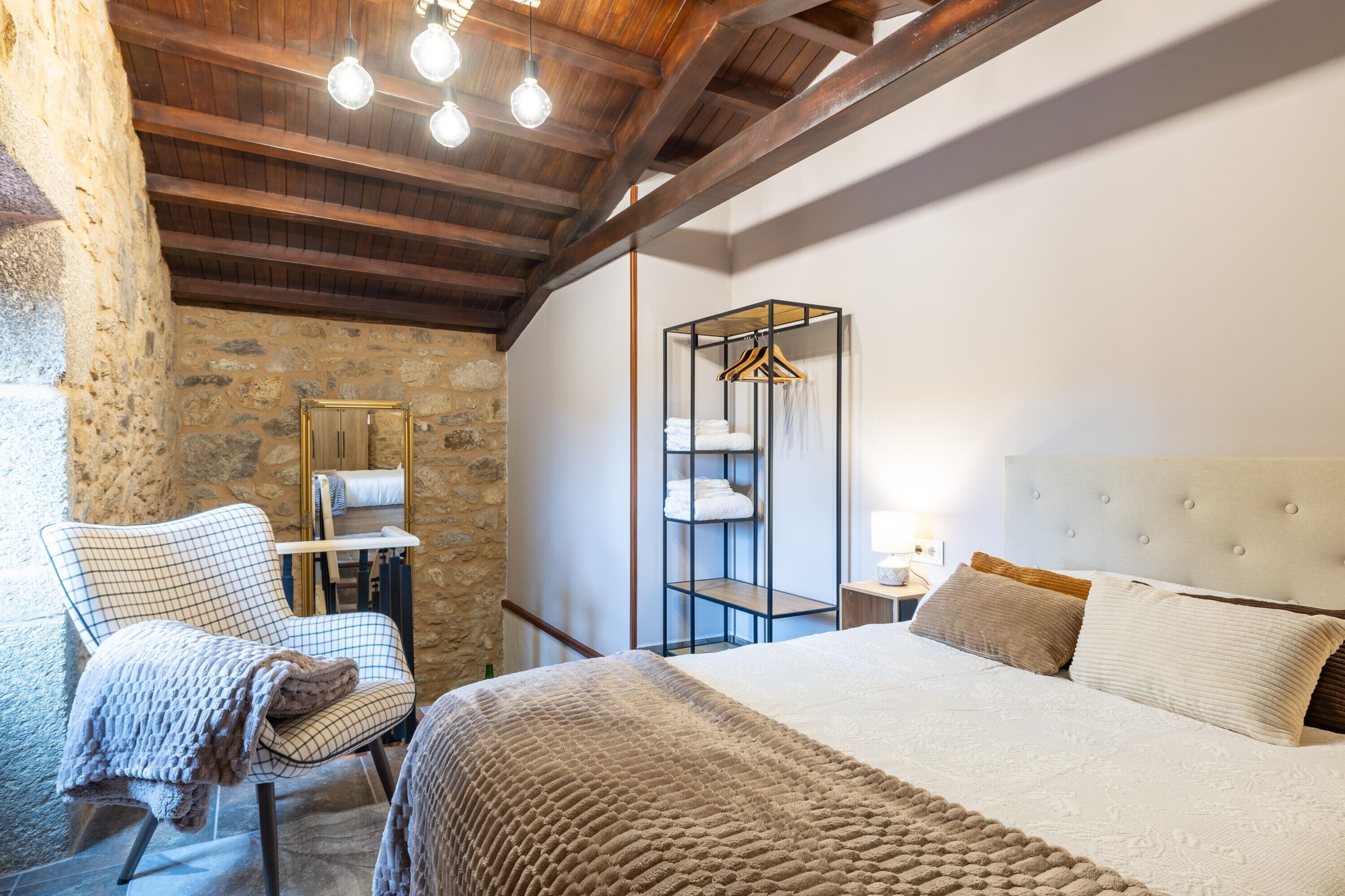 Ein Schlafzimmer mit einer Steinwand, einem Bett mit weißem Kopfteil, einem Sessel mit Decke und einem hängenden Kleiderschrank.