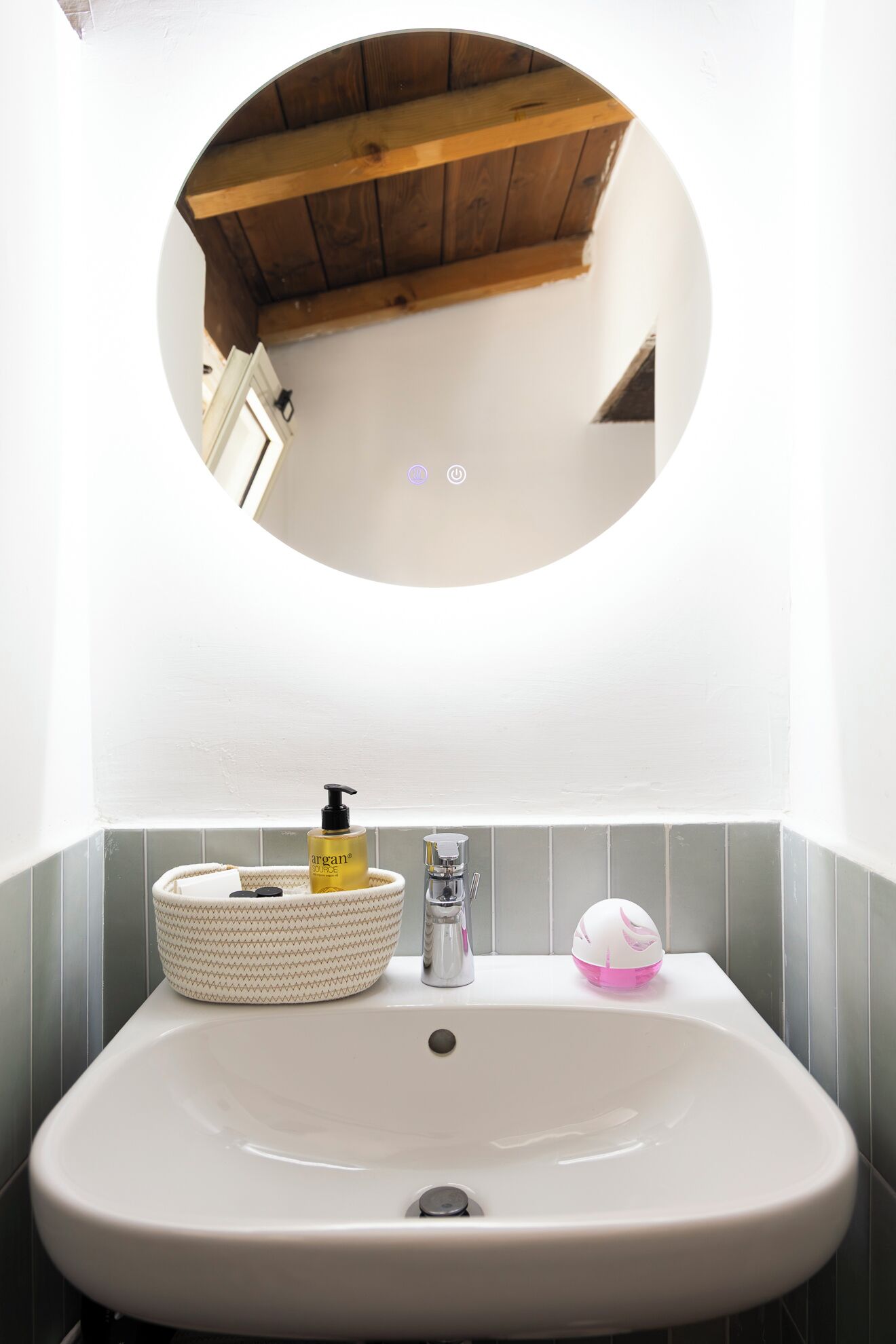Un bany amb un mirall rodó, un lavabo i un vàter.