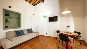 A room with a sofa, a dining table with chairs, a TV, and a green shelf.