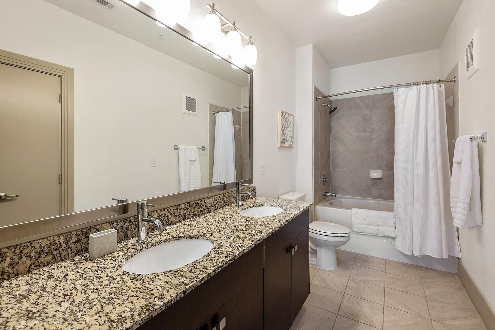 Une salle de bain avec deux lavabos, des toilettes, une douche et un grand miroir.