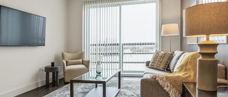 Una sala de estar moderna con un sofá, un sillón, una mesa de centro de vidrio y un televisor montado en la pared.