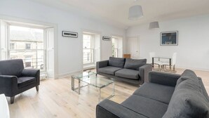 Una sala de estar moderna con un sofá gris, una mesa de centro de cristal y un comedor con una mesa y sillas de cristal.