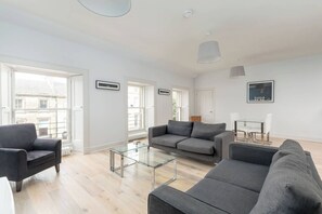 Ein modernes Wohnzimmer mit einem grauen Sofa, einem Glastisch und einem Essbereich mit einem Tisch und Stühlen.