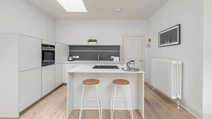 Una cocina moderna con armarios blancos, una isla central con taburetes, horno empotrado y radiador.