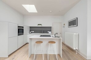 Eine moderne Küche mit weißen Schränken, einer zentralen Kochinsel mit Sitzgelegenheiten, einem eingebauten Backofen und einer Heizung.