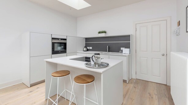 Una cocina moderna con una isla central, taburetes de bar, horno empotrado y una puerta blanca.