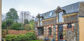 Ein zweigeschossiges Haus mit einer Naturstein-Fassade, einem Holzzaun und einem gepflegten Garten.