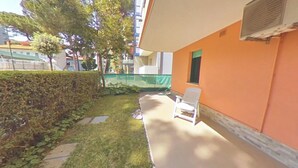 Een balkon met een witte stoel, een haag en een gebouw met een oranje muur en een raam.