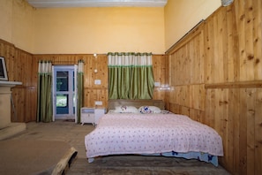 Une chambre avec des murs en bois, un lit recouvert d’une couvre-lit à motifs roses, une table de chevet et une fenêtre avec des rideaux verts.