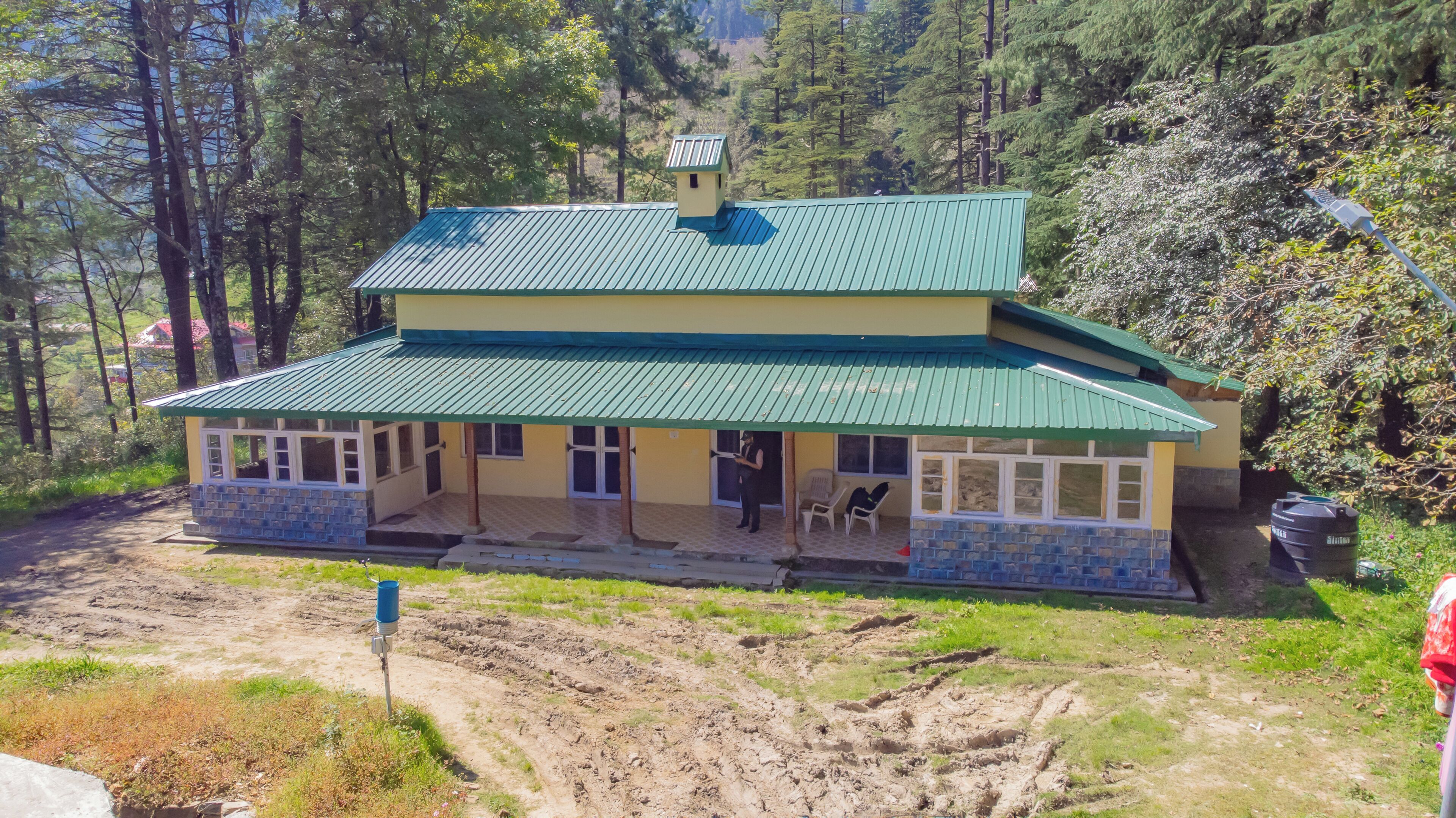 A two-story building with a green roof and a stone base, surrounded by trees.
