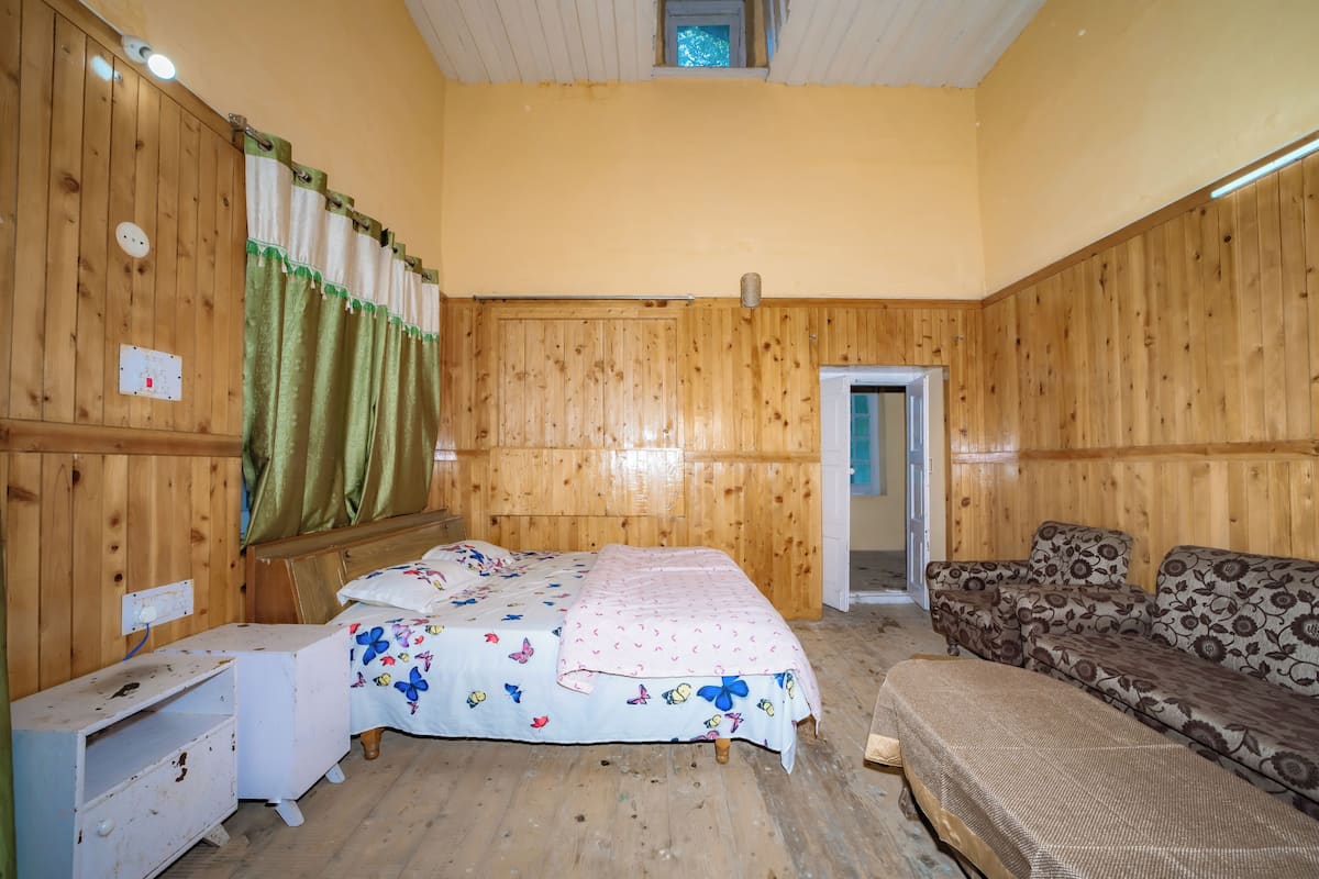 Habitació amb panells de fusta, un llit, un sofà, una tauleta de nit i una porta.