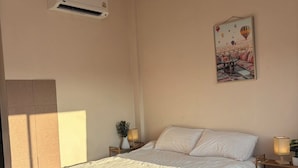 Quarto com cama, ar condicionado, mesa de cabeceira com abajur, quadro na parede e piso de mármore.