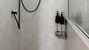 Chuveiro com chuveiro manual, painel de controle fixado na parede e janela com vista.