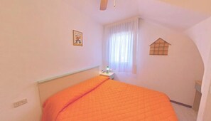 A bedroom with a bed, a nightstand, a window with curtains, and a small wall decoration. - Two-story Family Flat With Terrace (Lignano Sabbiadoro)