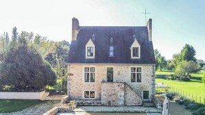 Ein Steinhaus mit steiler Dachneigung, zahlreichen Fenstern und einem Schornstein.