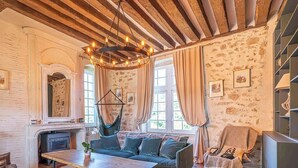 Ein rustikales Zimmer mit unverputzten Backsteinwänden, Holzbalkendecke, einer Couch, einem Tisch und einer Pendelleuchte.