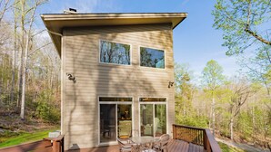 Ein zweigeschossiges Haus mit einer Terrasse, großen Schiebeglastüren und Blick auf den umgebenden Wald.