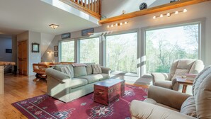 Ein geräumiges Wohnzimmer mit hoher Decke, großen Fenstern, einer Holztreppe und einer gemütlichen Sitzecke.