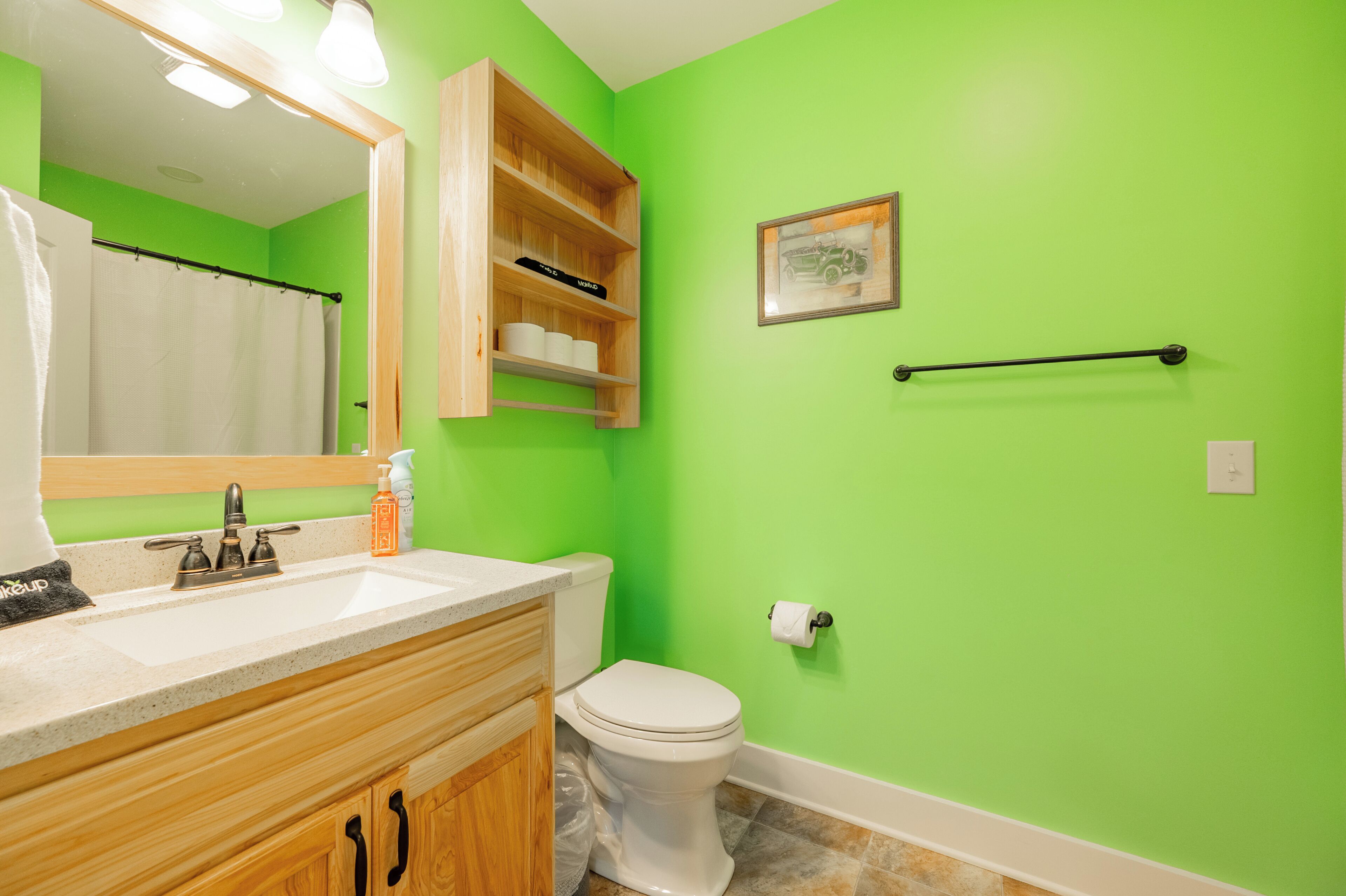 A bathroom with a green wall, wooden vanity, white toilet, and a towel rack.