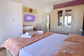 Ein Schlafzimmer mit Bett, Fernseher, Kleiderschrank und einem durchgehenden Türrahmen sichtbaren Badezimmer.