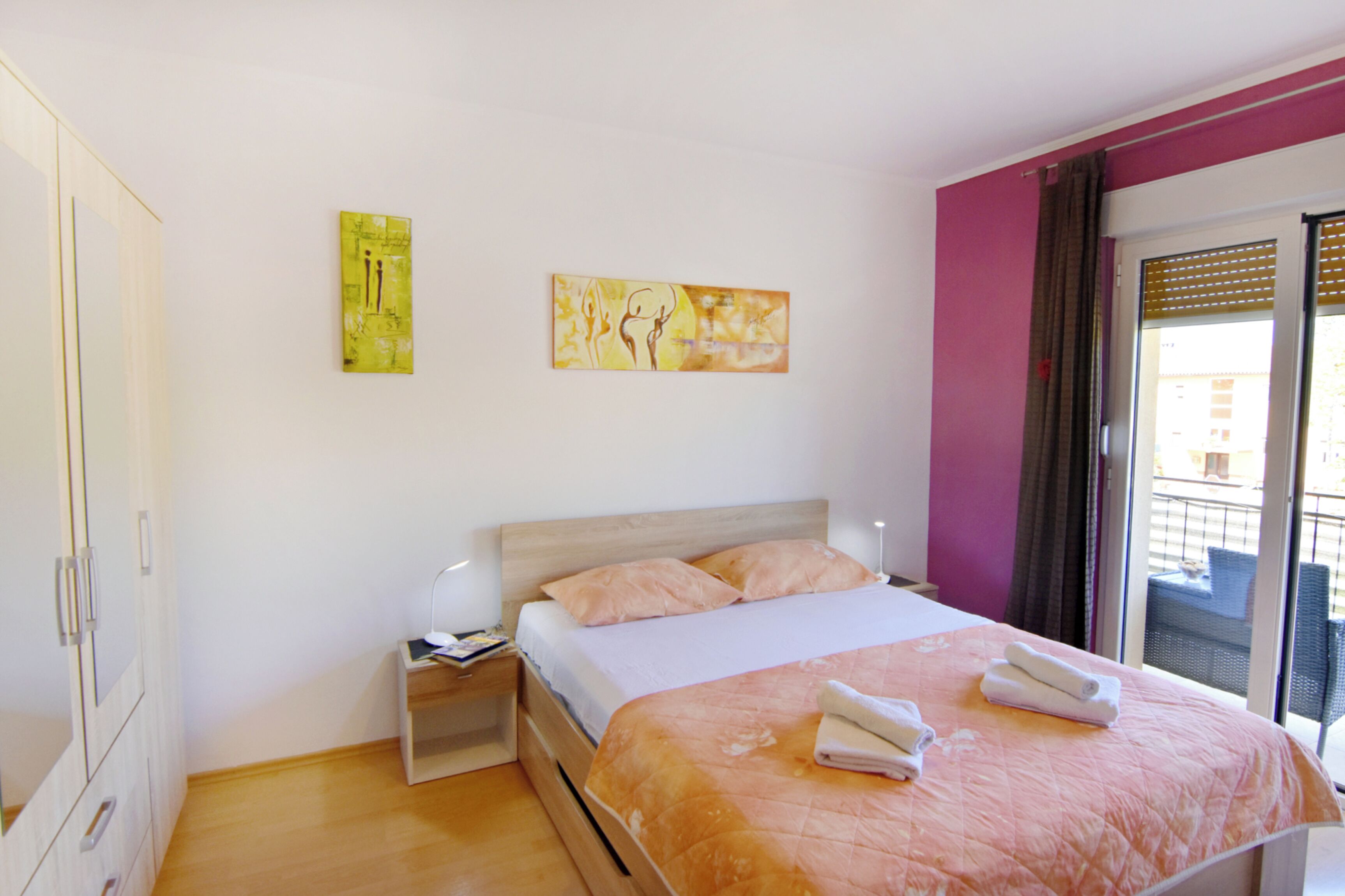 A bedroom with a bed, a nightstand, a wardrobe, and two paintings on the wall.