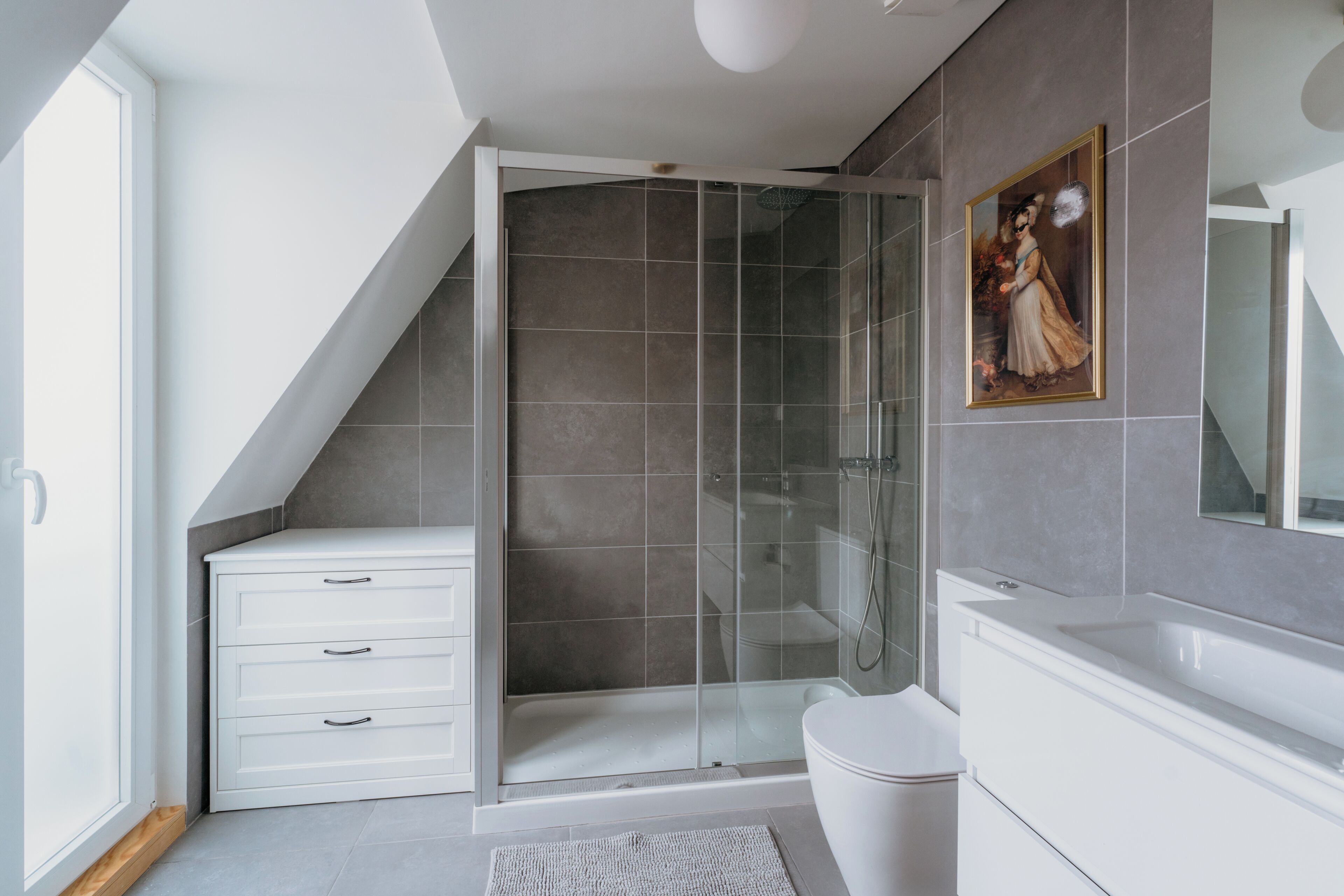 Un baño moderno con cabina de ducha de vidrio, tocador blanco y un espejo grande.