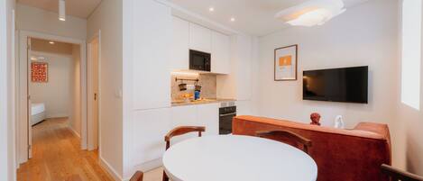 Una cocina moderna con armarios blancos, microondas y horno empotrado. Hay una zona de comedor con una mesa redonda y sillas de madera.