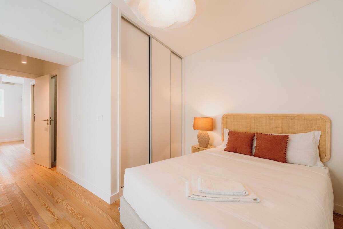 Habitación de hotel con cama, lámpara de noche y vista a un pasillo.
