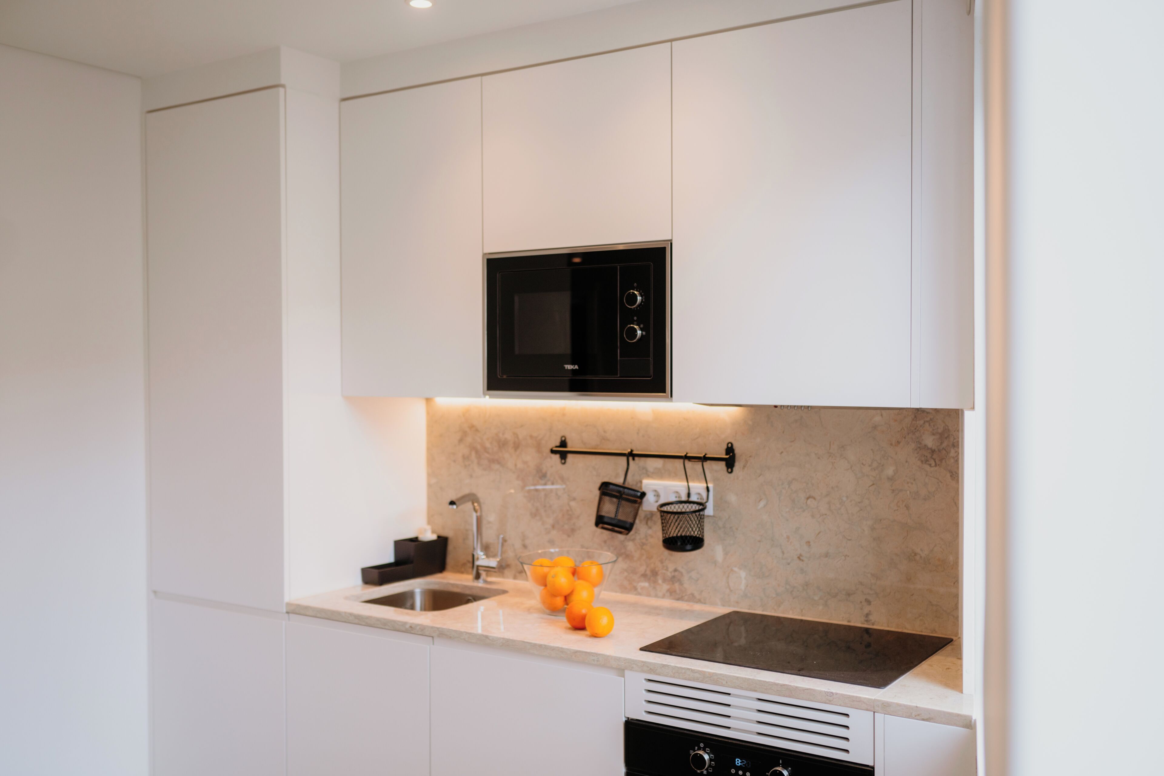 A modern kitchen with white cabinets, a black microwave, a sink, and a countertop with oranges.