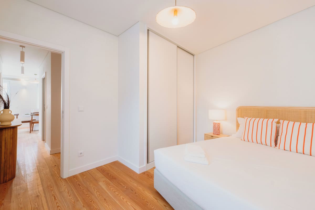Un dormitorio con cama, mesita de noche, lámpara y suelo de madera.