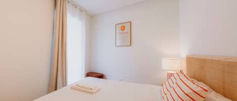 A hotel room with a bed, a bedside table, a lamp, a chair, and a wall-mounted picture.