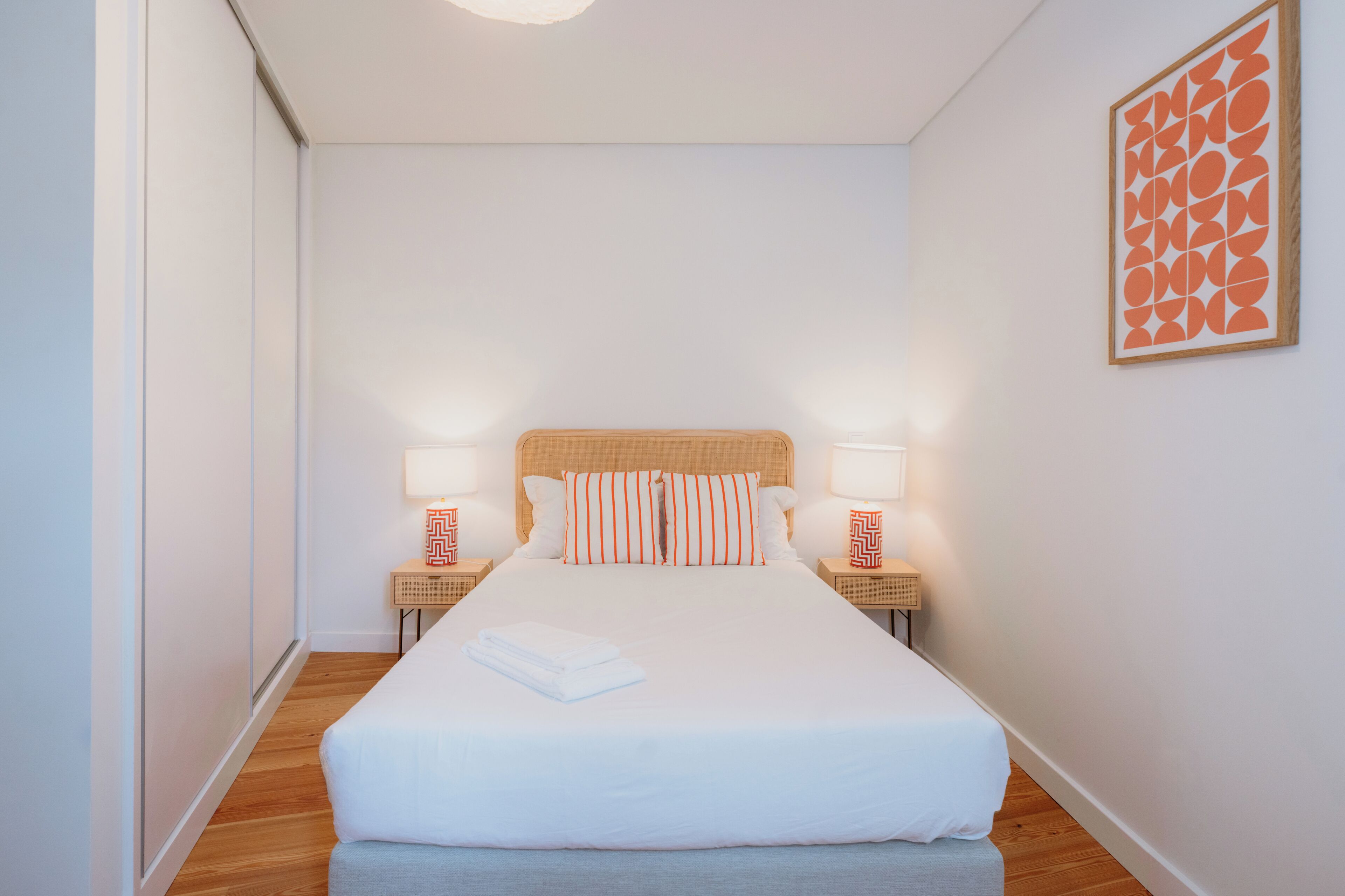 Un dormitorio con una cama grande, dos mesitas de noche con lámparas, un cabecero de madera y una obra de arte colgada en la pared.