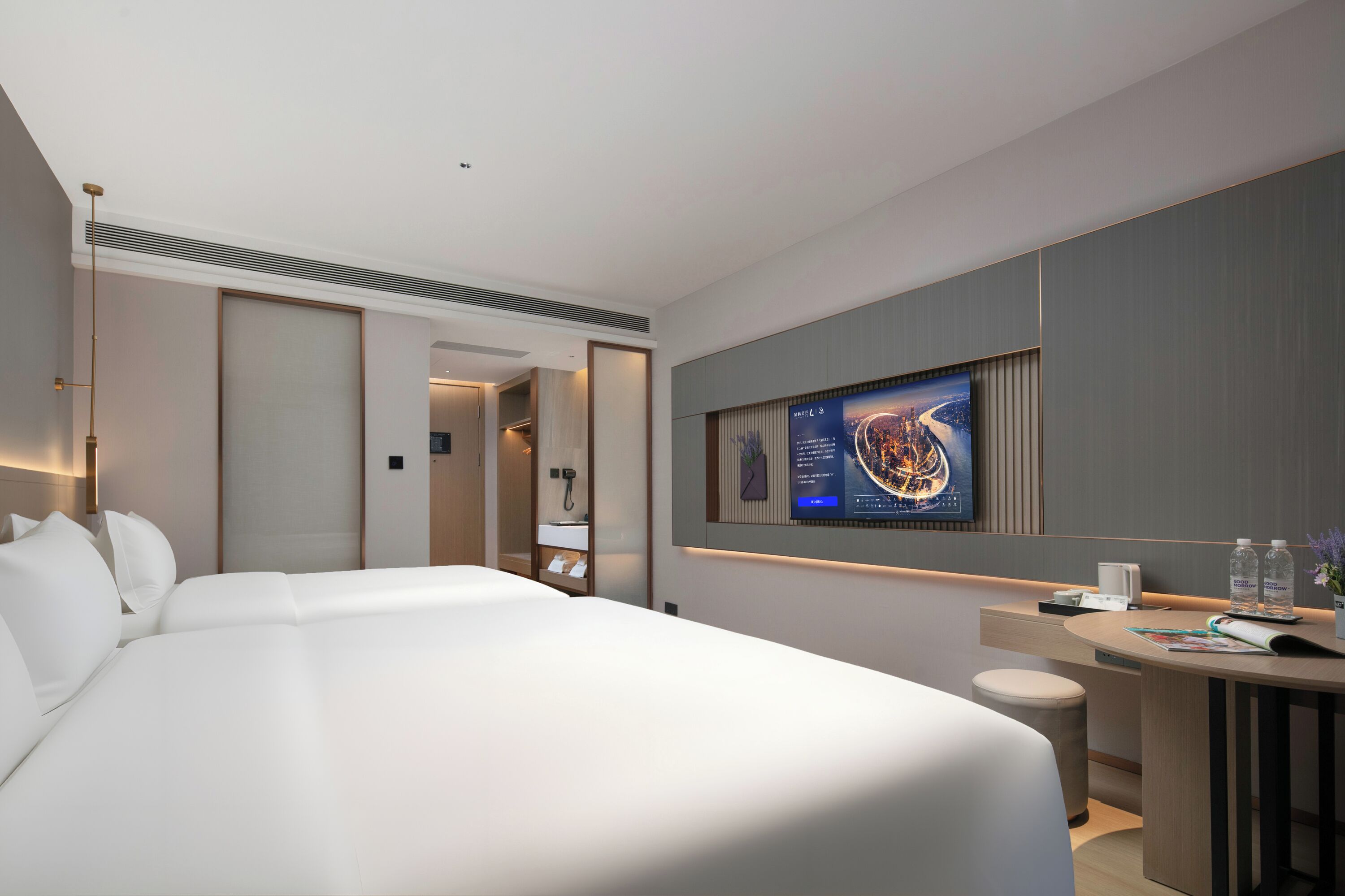 A modern hotel room with a large bed, a desk with a flat-screen TV, and a bathroom visible through an open door.