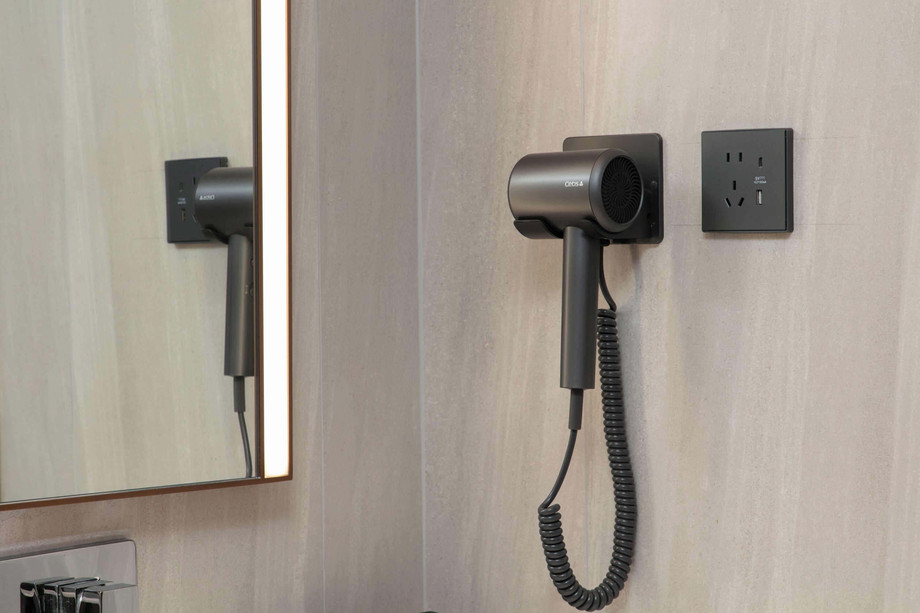 A hair dryer mounted on a wall with a power outlet and a switch.