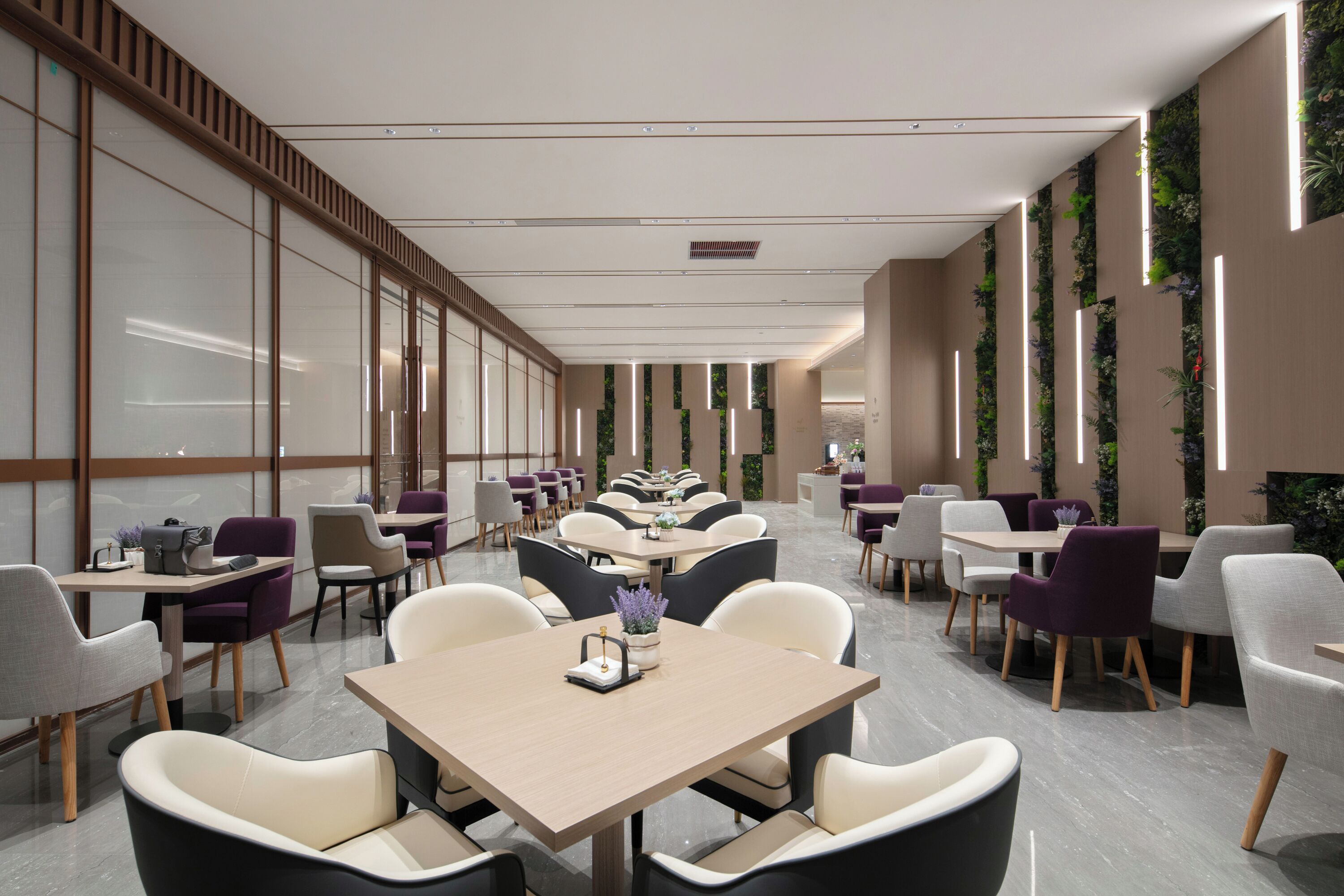 Un espace de restauration moderne, doté de plusieurs tables et chaises, d’un sol impeccable et de jardins verticaux sur les murs.