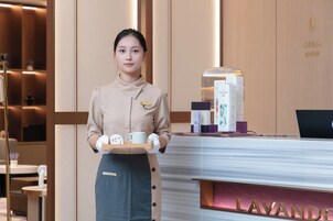 Zona de recepción de un hotel con mostrador identificado como 'LAVANDE', una máquina de café y una bandeja con una toalla enrollada y una taza.
