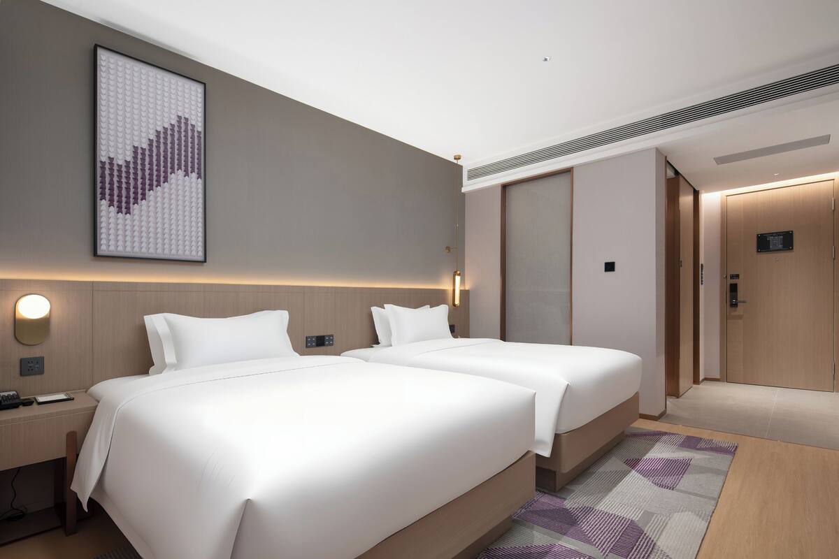 Habitación de hotel con dos camas, una mesita de noche, una obra de arte colgada en la pared, una lámpara y una puerta con un cartel.