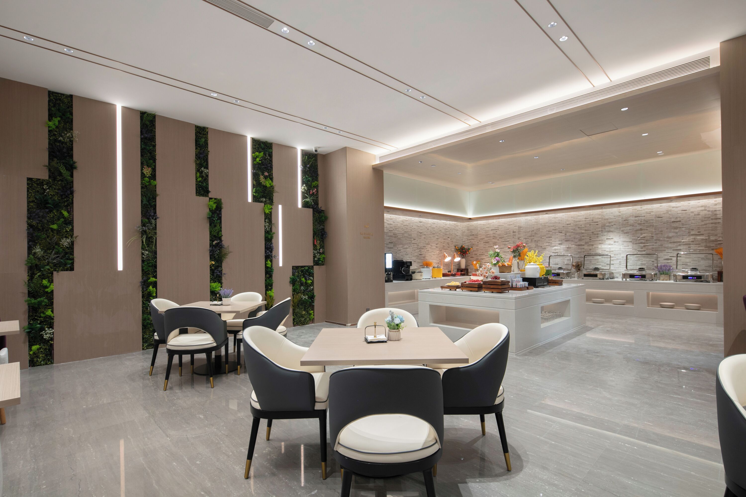 A modern hotel lobby with a central dining area, a kitchen counter, and vertical garden walls.