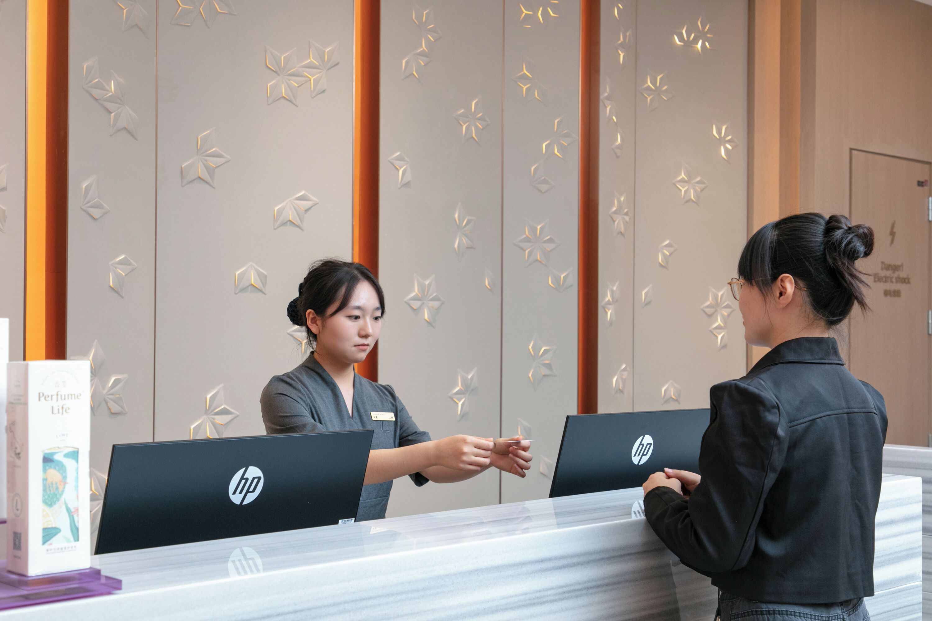 A reception desk with HP computers, a name tag, and a 'Danger Electric shock' sign.