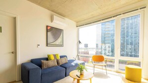 Un salon moderne avec un canapé, une table basse ronde, une plante et une vue sur la ville grâce à de grandes fenêtres.